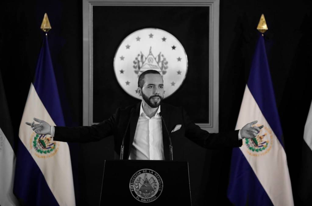 El Presidente Bukele con los brazos extendidos delante de la bandera de El Salvador
